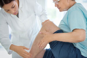 Closeup side view of female doctor massaging legs and calves of a senior female patient with visible varicose veins.